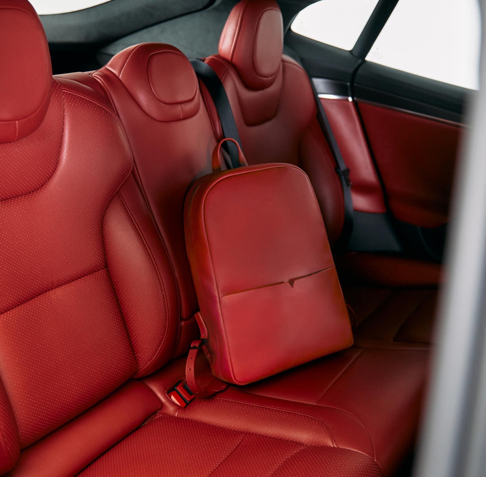 Back seat of a Tesla Model S with custom Serrano Red interior and matching backpack