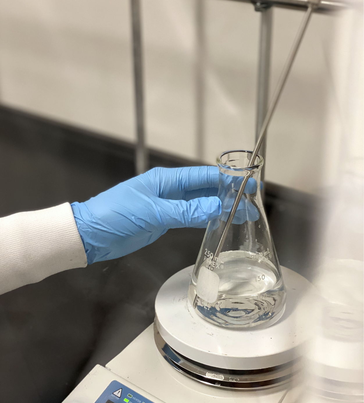 Chemist's hand holding beaker with clear liquid on a digital scale